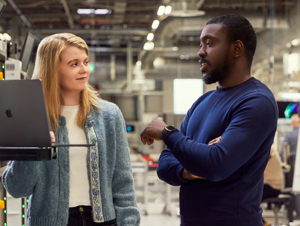 Membre des opérations et de l’approvisionnement d’Apple à Cork tenant un iPad tout en discutant avec une autre personne du service.