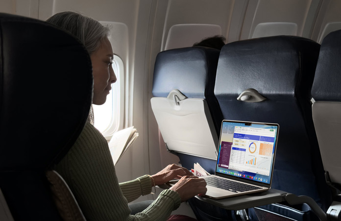 Henkilö istuu lentokoneessa ja työskentelee MacBook Airillaan