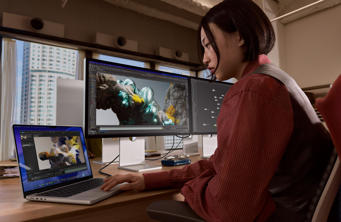 Seseorang di kantor bekerja menggunakan laptop MacBook yang terhubung ke Studio Display XDR melalui port Thunderbolt 5