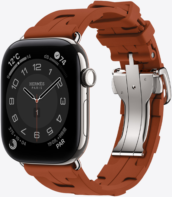 シルバーチタニウムケースのApple Watch Hermès Series 12、アナログデザインのCirculaireの文字盤に、時針、分針、秒針と、天気、ノイズ、アクティビティリング、パリの時間のコンプリケーションが表示されている。右側面の外観、Digital Crown、サイドボタン。キュイーヴル(ブラウン)のキリムシンプルトゥールストラップとの組み合わせ。成形ラバー素材、幾何学的に連なるデザイン、シルバーのメタルクラスプ