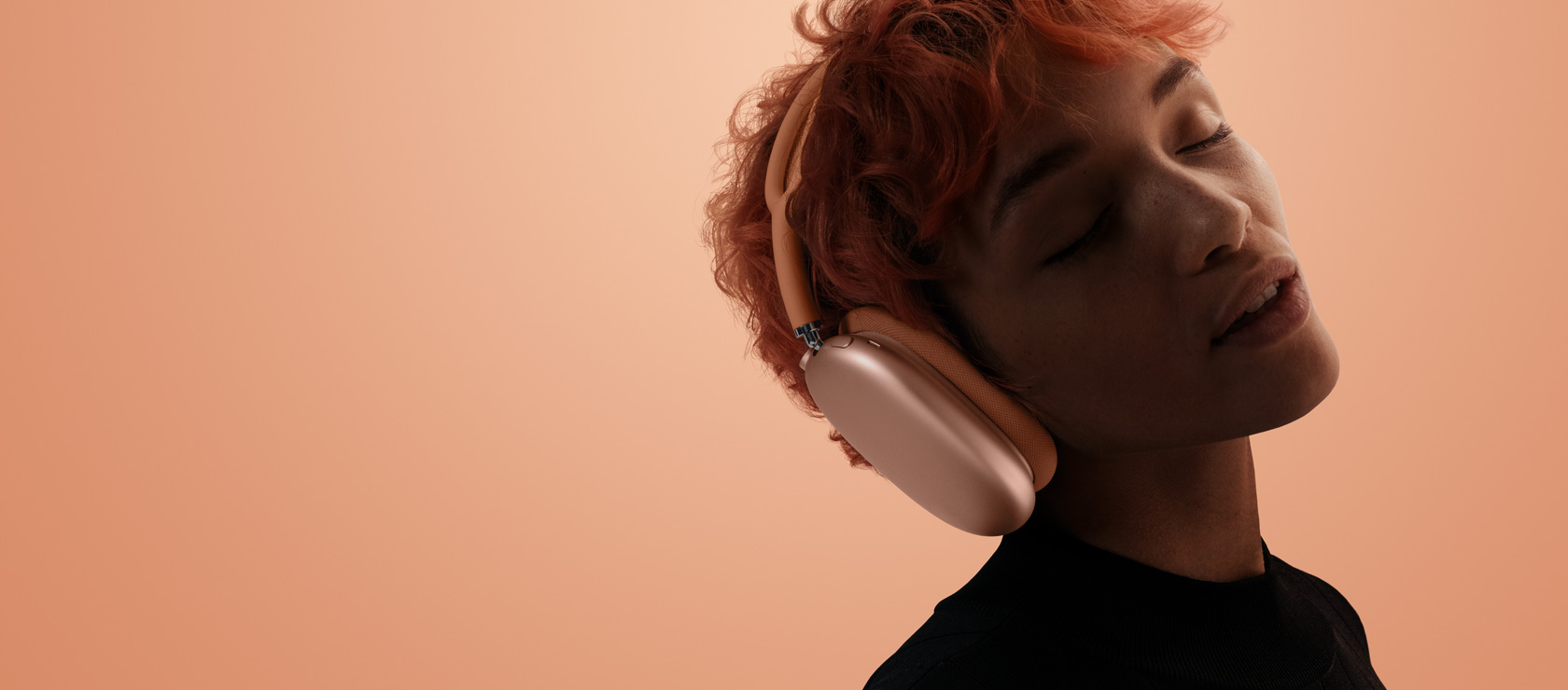 Kallutatud pea ja suletud silmadega inimene kandmas AirPods Max 2 kõrvaklappe, oranžis toonis, oranžikasroosal taustal