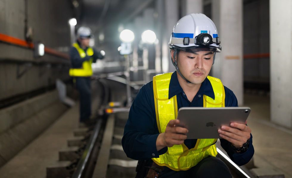 東京メトロのトンネルで、安全ベストとヘルメットを着用した作業員がiPadを見ながら保守作業を進めている
