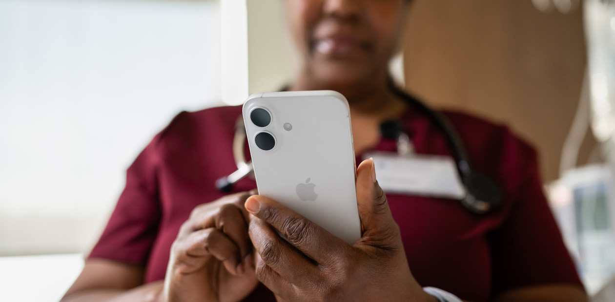 En kvindelig sygeplejerske i rød uniform kigger på sin iPhone.