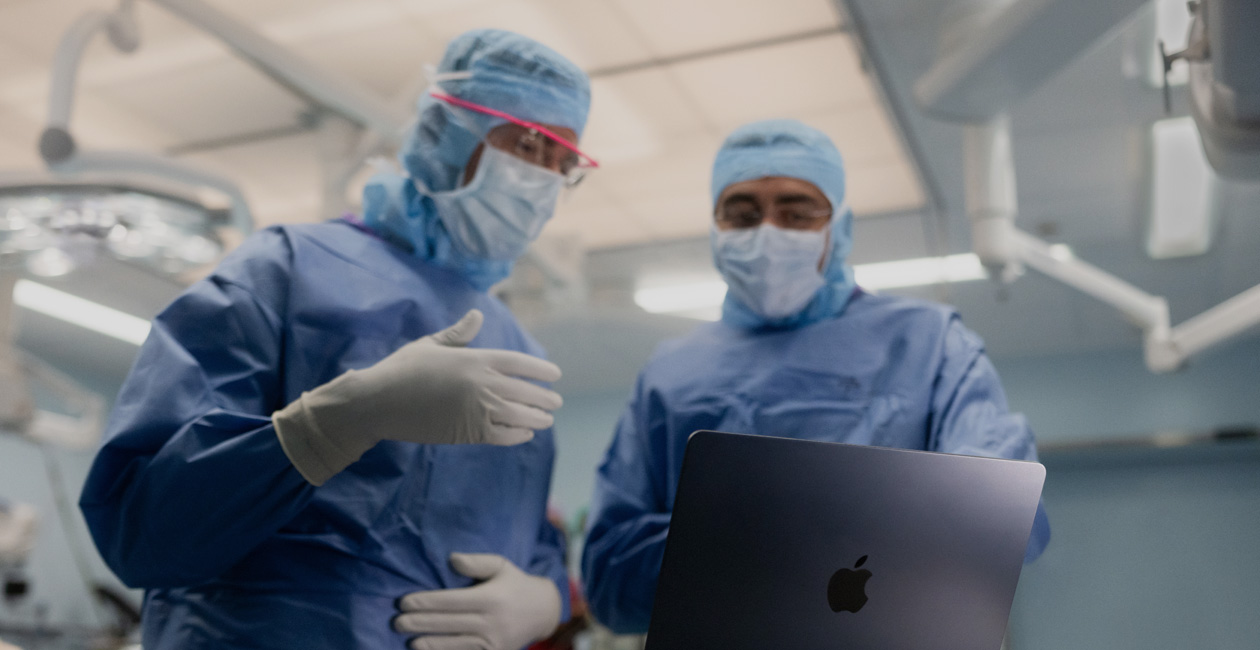 Hai bác sĩ phẫu thuật đang thảo luận về một nội dung trên màn hình của MacBook Pro trong phòng phẫu thuật.