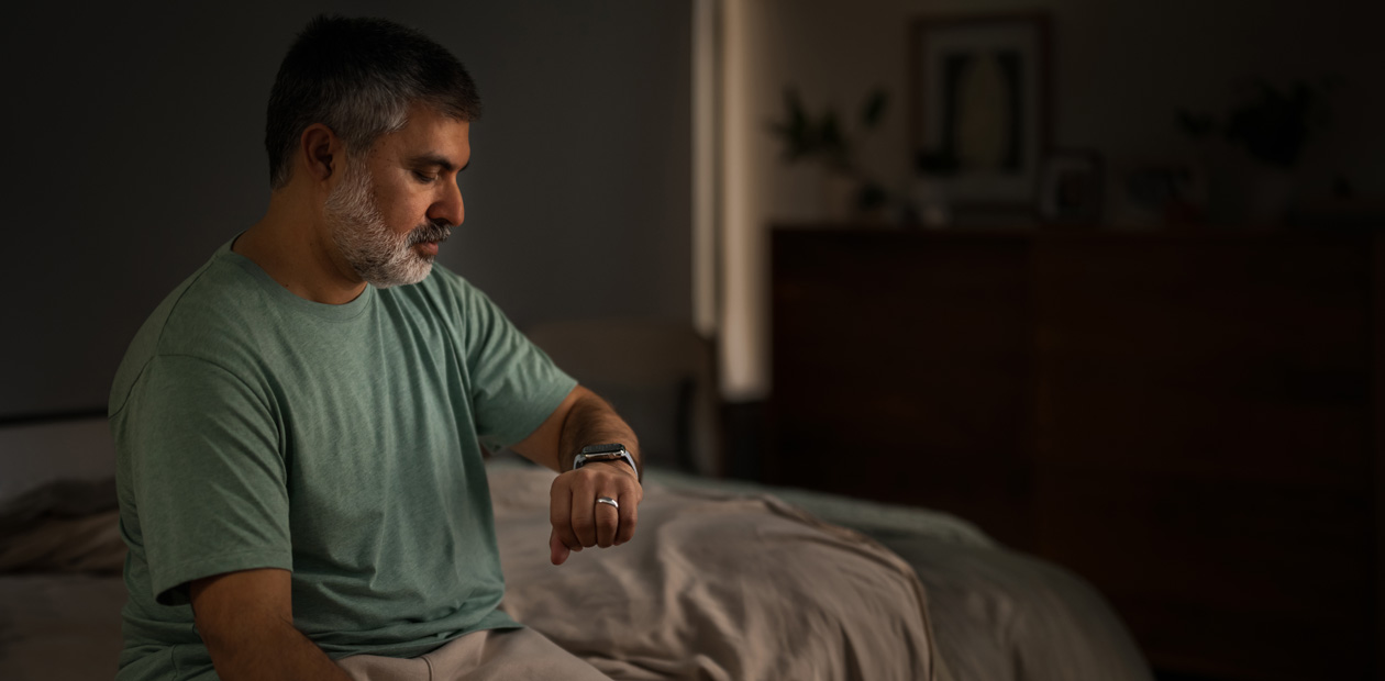 En mann sitter i sengen og sjekker Apple Watch.