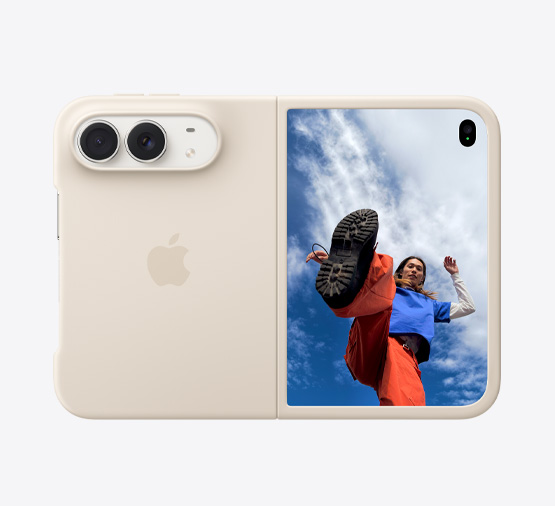 Un iPhone Duo color bianco stellare in una custodia in silicone color sabbia, posizione orizzontale, completamente aperto, si nota la doppia fotocamera Dual Fusion in alto a sinistra, la custodia copre la parte posteriore e i bordi del display frontale, sul lato destro si nota il display esterno con l’immagine di una persona in piedi sotto a un cielo blu nuvoloso