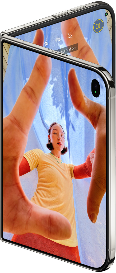 iPhone Duo, Yıldız Rengi, hafifçe açık, dış ekranda Kamera uygulaması ve Center Stage ön kamera gösteriliyor, iç ekranda Fotoğraflar uygulaması arşivi gösteriliyor