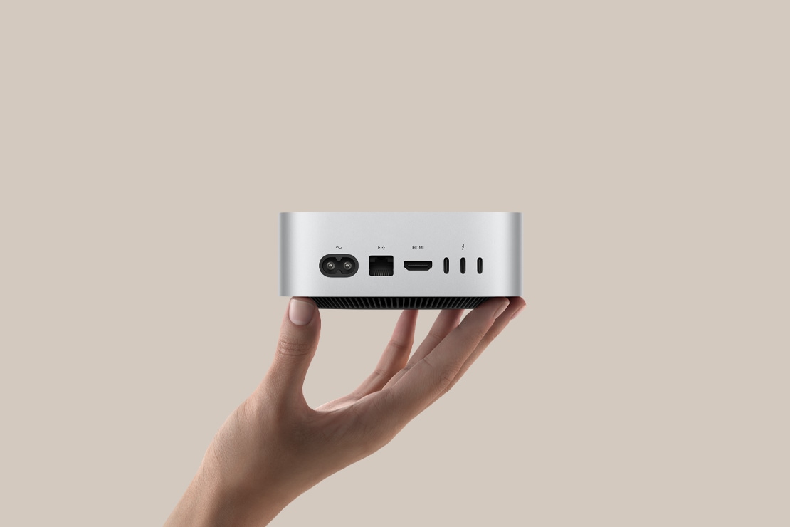 Ant pirštų galiukų laikomas sidabro spalvos „Mac mini“ su galiniais prievadais