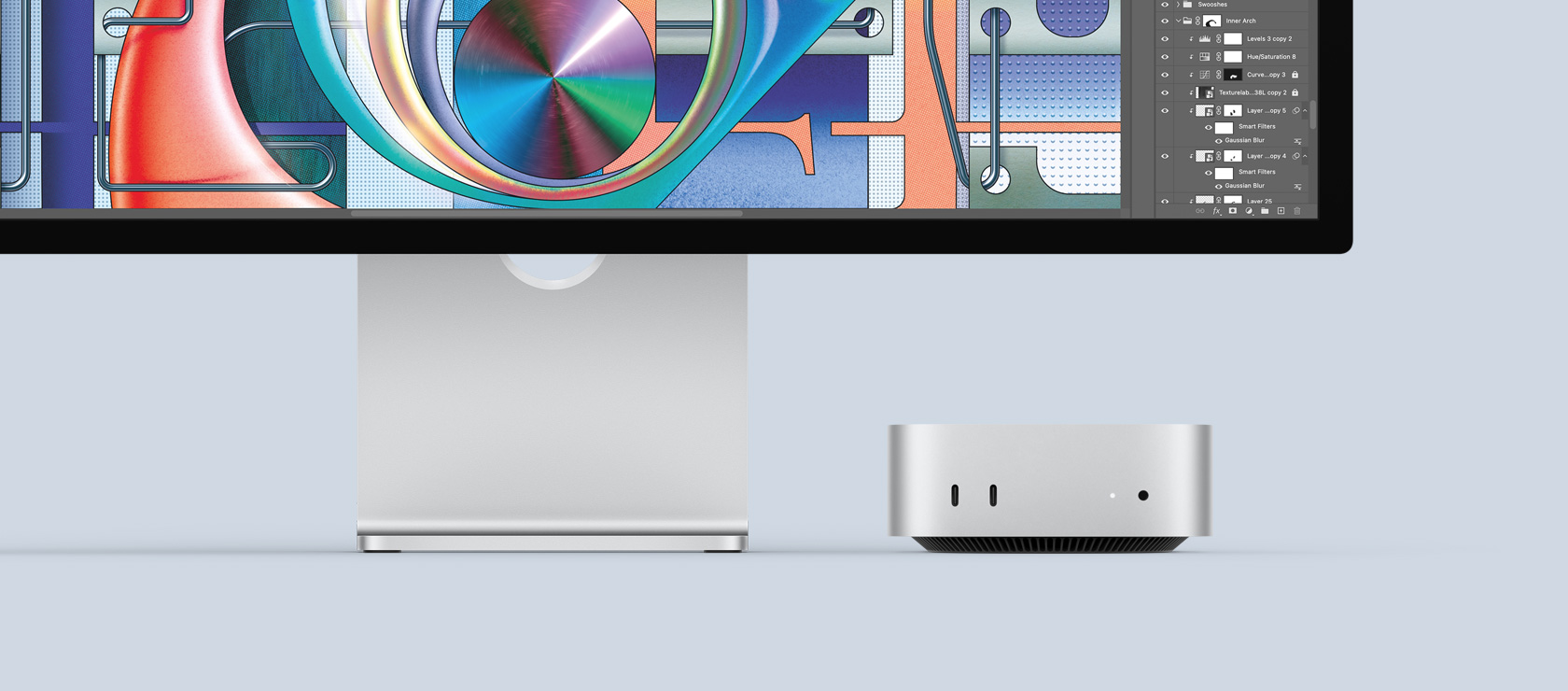 Sidabro spalvos „Mac mini“ vaizdas iš priekio, kuriame matyti priekiniai prievadai bei indikatorinė lemputė ir kuris dailiai įkomponuotas po „Mac“ monitoriumi, kuriame matomas spalvingas ekranas